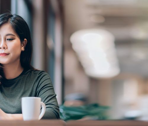 A woman is sitting in front of a window, engaging in change management as she looks at her laptop.